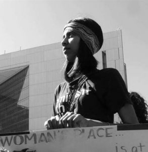 A black and white photo of a young woman holding up a sign.