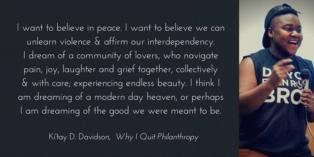 Black youth is smiling with an open mouth and snapping in celebration of a great comment by an audience member while facilitating a Disability History, Culture, and Pride workshop for youth with disabilities during the summer of 2014. Ki'tay is holding a microphone in his left hand and snapping with his right. He is wearing a black shirt, orange pants and a faux leather black hat turned backwards. 