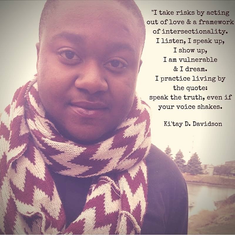 Photo of a black youth pensively looking into the camera, wearing a black shirt and knitted chevron scarf. standing in front of a small body of water with pine trees, houses and the sky as the backdrop. The above quote is written in dark letters in the sky on the right hand side of the photo. Quote included in the caption.