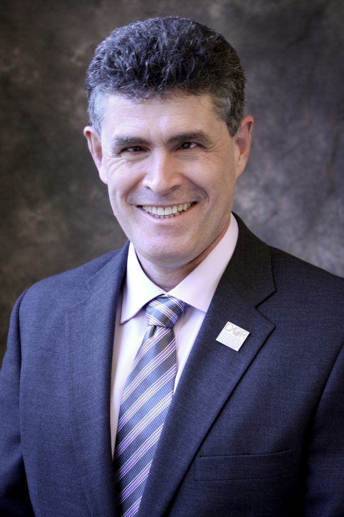 Closeup photo of a Portuguese man wearing a suit and tie, smiling.